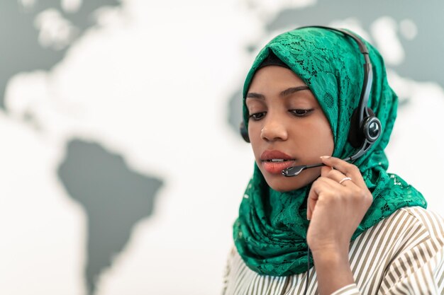 Mulher afro muçulmana com lenço verde hijab empresária representante do cliente com fone de ouvido ajudando e apoiando on-line com o cliente em um call center moderno. foto de alta qualidade