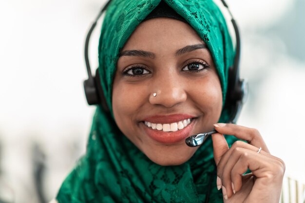 Mulher afro muçulmana com lenço verde hijab empresária representante do cliente com fone de ouvido ajudando e apoiando on-line com o cliente em um call center moderno. Foto de alta qualidade