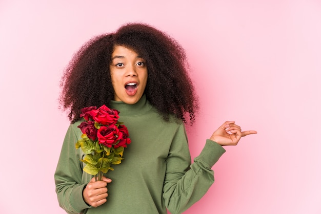 Mulher afro nova mantendo rosas isoladas. Jovem mulher afro segurando uma rosas apontando para o lado