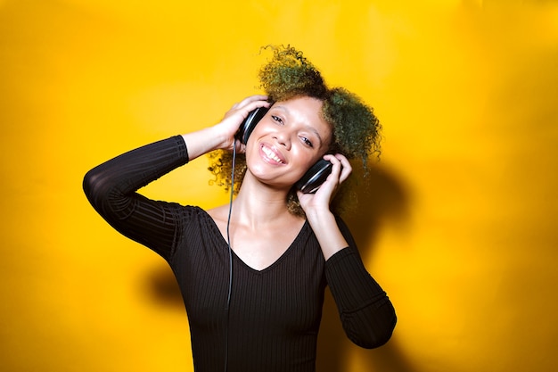 Mulher afro ouvindo música com fones de ouvido em fundo colorido