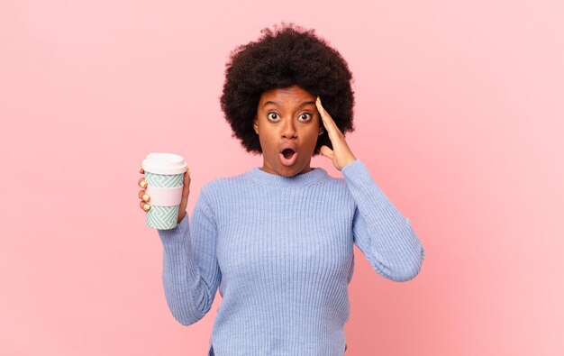 Mulher afro parecendo feliz, atônita e surpresa, sorrindo e percebendo uma boa notícia incrível. conceito de café