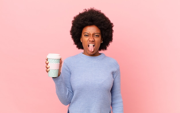 Mulher afro se sentindo enojada e irritada, mostrando a língua, não gostando de algo nojento e nojento. conceito de café