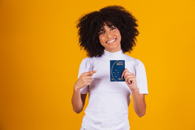 Foto mulher afro segurando um passaporte brasileiro nas mãos.