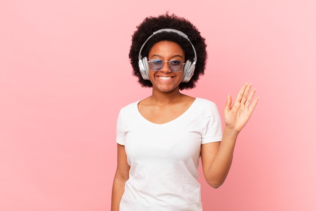 Mulher afro sorrindo com alegria e alegria, acenando com a mão, dando as boas-vindas e cumprimentando ou dizendo adeus. conceito de musica