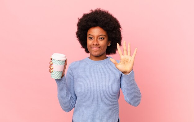 Mulher afro sorrindo e parecendo amigável, mostrando o número cinco ou quinto com a mão para a frente, em contagem regressiva. conceito de café