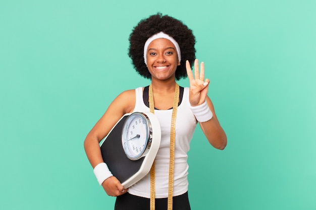 Mulher afro sorrindo e parecendo amigável, mostrando o número três ou terceiro com a mão para a frente, conceito de dieta em contagem regressiva