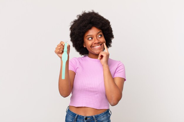 Mulher afro sorrindo feliz e sonhando acordada ou duvidando, olhando para o conceito de relógio lateral