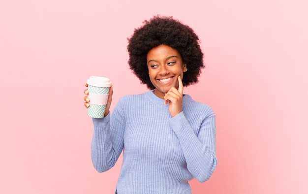 Mulher afro sorrindo feliz e sonhando acordada ou duvidando, olhando para o lado. conceito de café