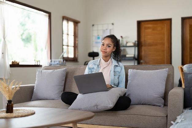 Mulher afroamericana de retrato trabalhando no laptop sentado no sofá em casa