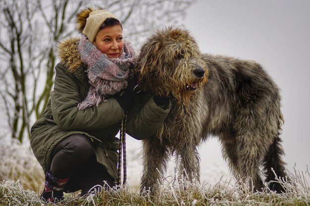 Foto mulher agachada por cão-lobo irlandês no campo durante o inverno