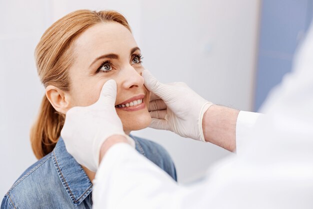 Mulher agradável e agradável olhando para o médico e sorrindo enquanto está de bom humor