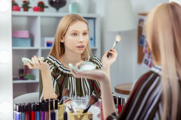 Mulher agradável e agradável se maquiando enquanto se prepara para sair