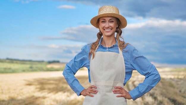 Foto mulher agricultora, chapéu de palha, avental em pé, fazenda, sorrindo