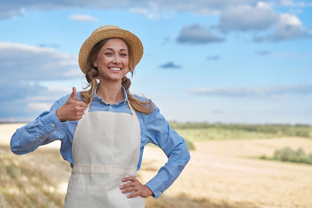 Foto mulher agricultora, chapéu de palha, avental em pé, fazenda, sorrindo