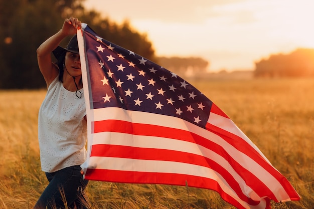Mulher agricultora no campo agrícola com a bandeira americana no pôr do sol