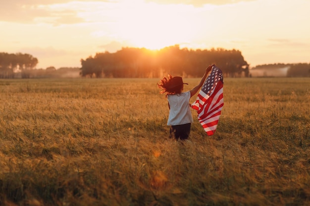 Mulher agricultora no campo agrícola com a bandeira americana no pôr do sol