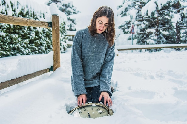 Mulher ajoelhada em uma paisagem de neve com um relógio nas mãos