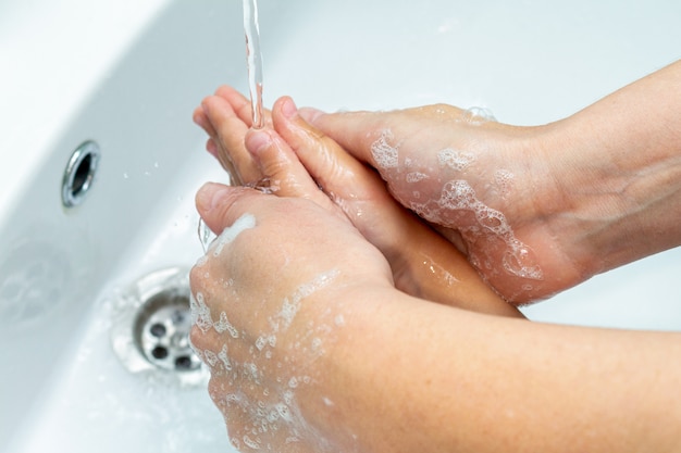 Mulher ajuda as crianças a lavar as mãos sob o close-up da torneira