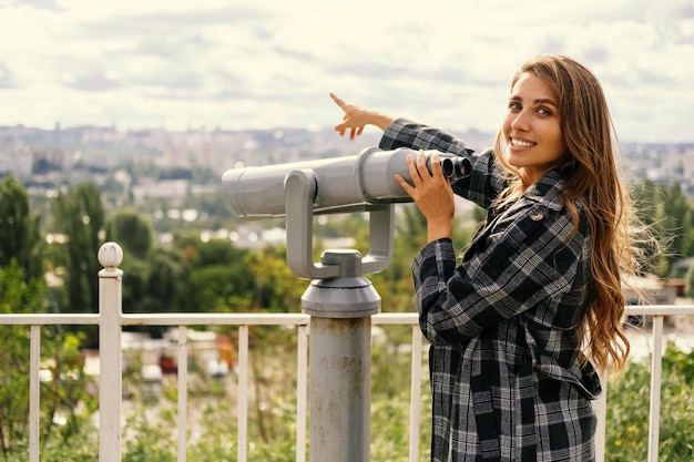 Mulher alegre aponta para a cidade que ela estava olhando em binóculos turísticos