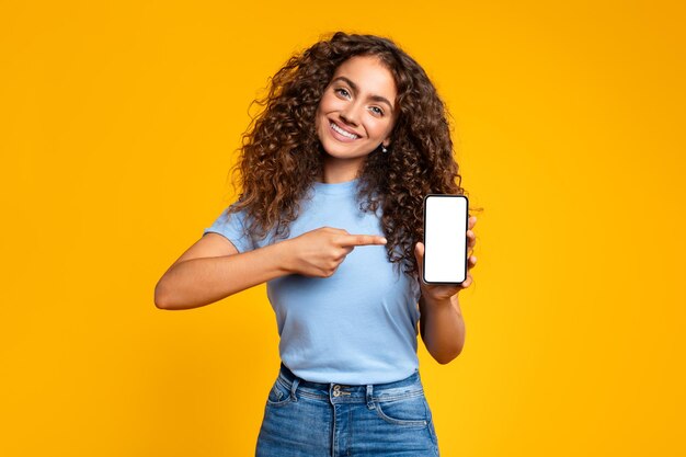 Mulher alegre apontando para a tela do smartphone em amarelo