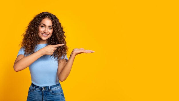 Foto mulher alegre apresentando com a mão no espaço livre amarelo