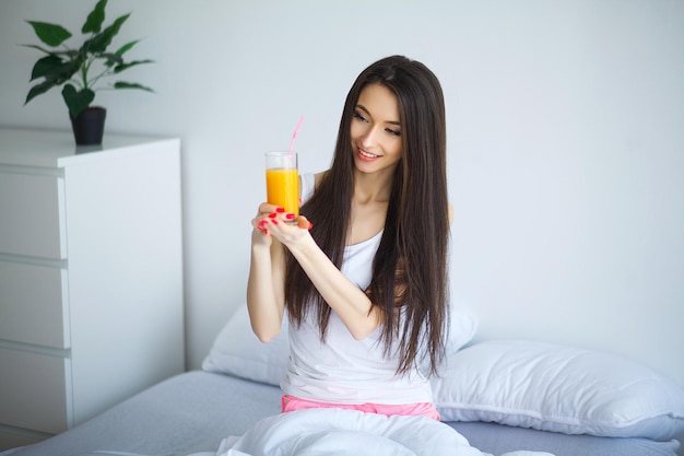 Mulher alegre bebendo suco de laranja sentada na cama