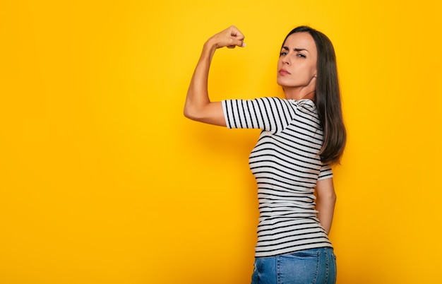 Mulher alegre, bonita e forte, mostra o bíceps isolado em um fundo amarelo