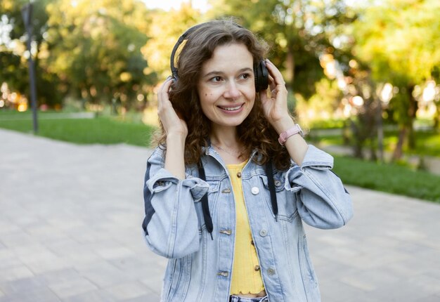 Mulher alegre carismática de cabelo encaracolado de meia-idade ouvindo música em fones de ouvido na cidade