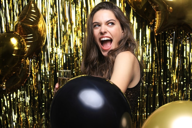 Mulher alegre com balões rindo sobre fundo dourado.