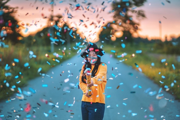 Mulher alegre com confetes coloridos de pé na estrada durante o pôr do sol