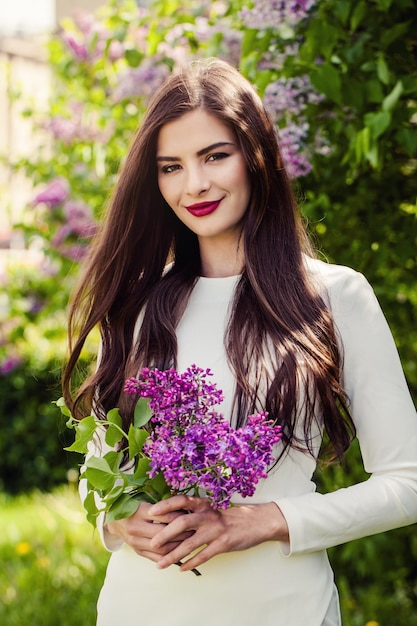 Mulher alegre com flores lilás de primavera ao ar livre modelo de moda menina morena feliz