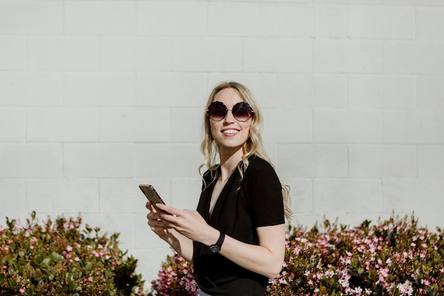Mulher alegre com óculos de sol enviando mensagens de texto no telefone