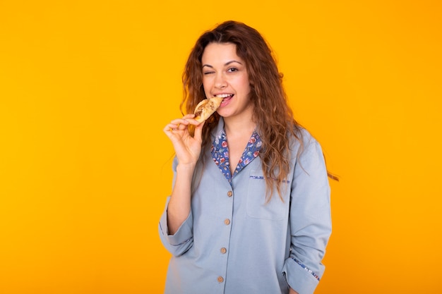 Mulher alegre com pijama da moda vai comer um pequeno e delicioso croissant no fundo amarelo