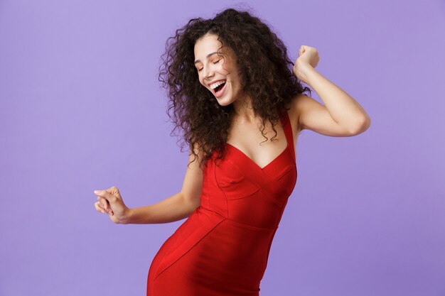 mulher alegre com vestido vermelho, sorrindo e dançando, isolada sobre a parede violeta