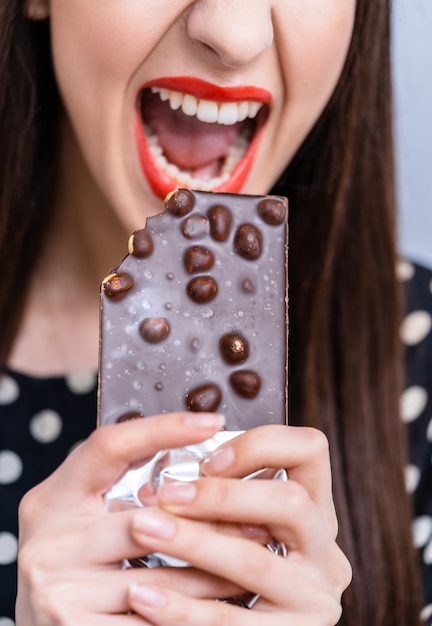 Mulher alegre comendo chocolate. Foto recortada. Fechar-se. Chocolate preto com nozes.