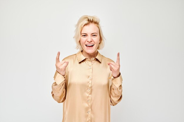 Mulher alegre de blusa bege fazendo gesto de mão rock and roll isolado em um fundo claro