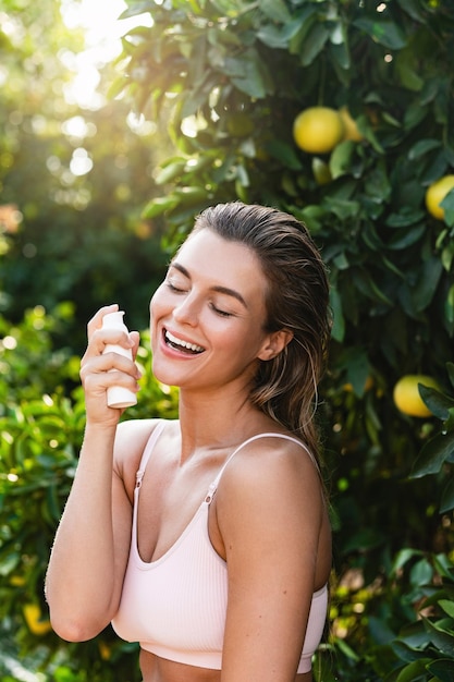 Mulher alegre e bonita aplicando creme hidratante ou protetor solar na pele facial