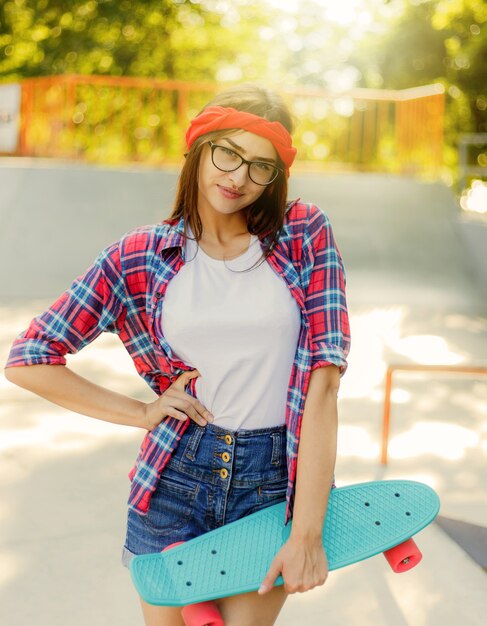 Mulher alegre e emocional jovem hippie vestida com roupas elegantes segurando o skate no skatepark em um dia ensolarado