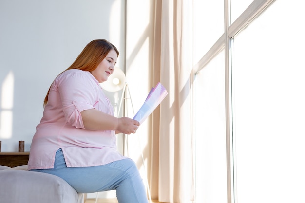 Mulher alegre e positiva segurando uma revista enquanto se concentra na leitura