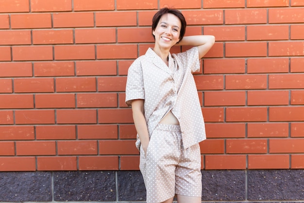 Mulher alegre em casa usa pijama ao ar livre parede de tijolo emoções copia espaço e lugar vazio para roupa de dormir de texto e conceito de homewear