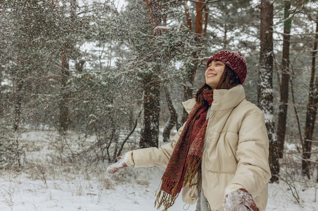 Mulher alegre em roupas quentes de inverno jogando neve e aproveitando o clima enquanto passa o tempo na floresta