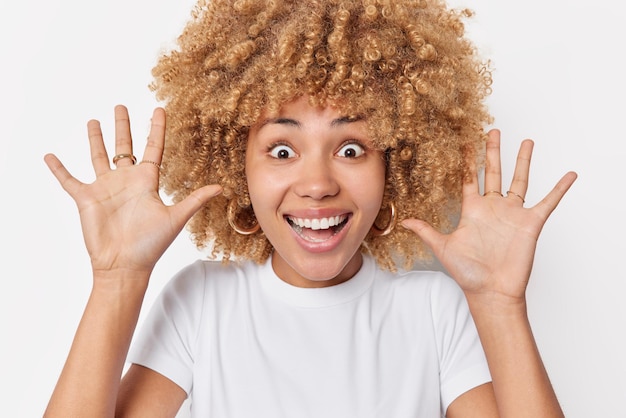 Mulher alegre otimista mantém palmas levantadas sorrisos expressa emoções positivas vestida com roupas casuais tem olhos cheios de felicidade isolados sobre fundo branco. Emoções humanas positivas