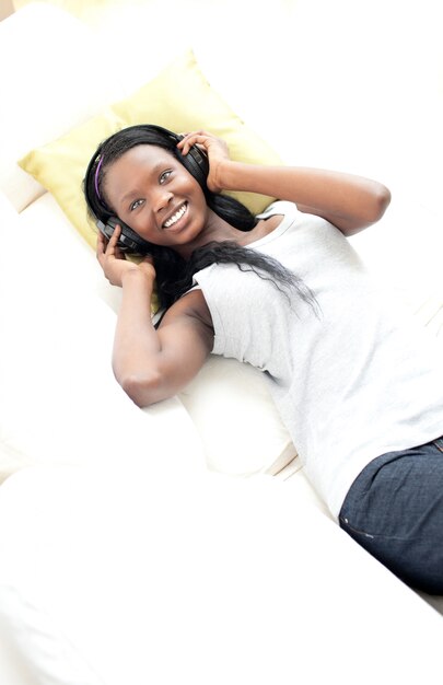 Mulher alegre ouvindo música com fones de ouvido deitado em um sofá