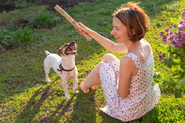 Mulher alegre positiva brincando com seu amado cachorro jack russell terrier no quintal de sua casa de campo em um dia ensolarado de verão. conceito de amor pelos animais e recreação familiar.