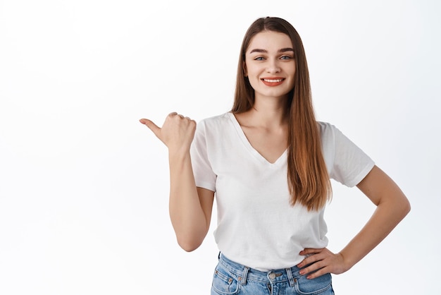 Mulher alegre sorridente aponta o polegar para a esquerda mostra espaço de cópia propaganda loja acordo promocional parece determinado recomendar suportes de produtos contra fundo branco