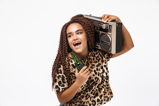 mulher alegre, sorrindo e segurando uma caixa de som vintage com fita cassete no ombro, isolada contra uma parede branca