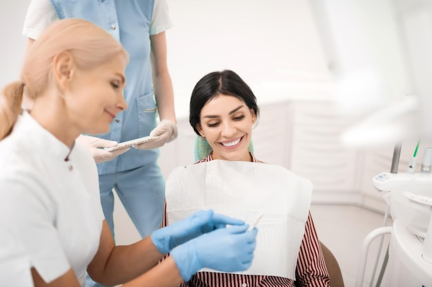 Mulher alegre sorrindo olhando para dentes clareando amostras dentista mostrando a ela