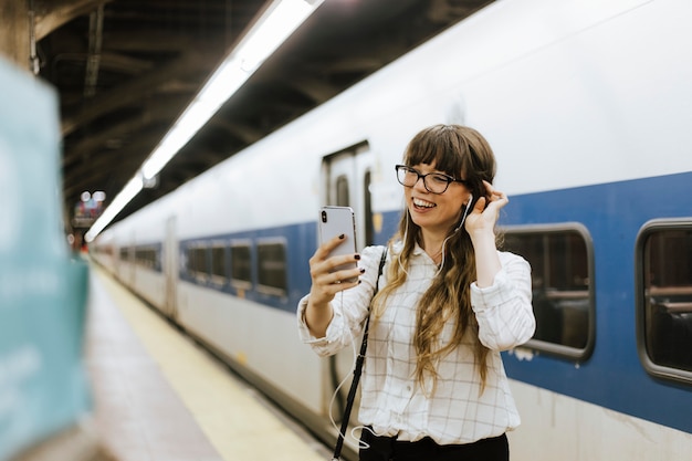 Mulher alegre, tendo uma chamada de vídeo em uma plataforma de metrô