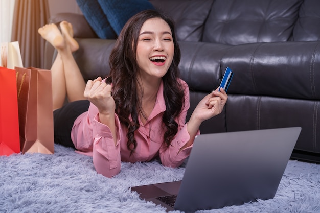 Mulher alegre usando laptop para fazer compras on-line com cartão de crédito na sala de estar bem sucedida