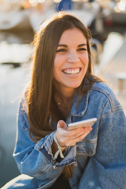 Foto mulher alegre usando o telefone enquanto está sentada ao ar livre